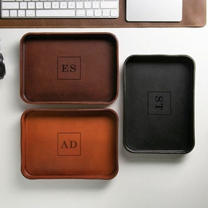 May include: Three leather trays with personalized initials. The trays are brown, tan, and black. The initials are "ES", "AD", and "ST".
