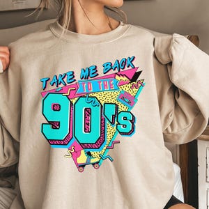 Puede incluir: Una sudadera beige con un estampado gr&aacute;fico que dice "Take Me Back To The 90's" en un estilo retro colorido. El gr&aacute;fico incluye una cinta de casete, patines y formas geom&eacute;tricas.