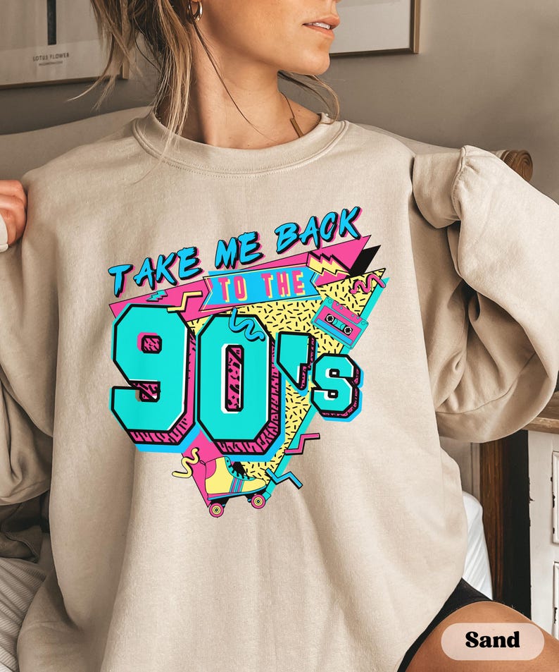 Puede incluir: Una sudadera beige con un estampado gr&aacute;fico que dice "Take Me Back To The 90's" en un estilo retro colorido. El gr&aacute;fico incluye una cinta de casete, patines y formas geom&eacute;tricas.