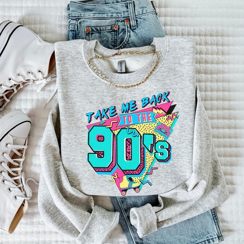 Puede incluir: Una sudadera gris con un estampado gr&aacute;fico que dice "Take Me Back To The 90's" en un estilo retro colorido. El gr&aacute;fico incluye una cinta de casete, patines y formas geom&eacute;tricas.