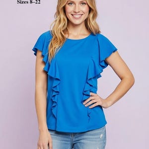 May include: A white ceramic mug with a black handle and the text "But First, Coffee" in a bold, black font. The mug is set against a blurred background. The mug appears to be approximately 10 cm tall.