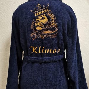 May include: Navy blue terry cloth robe with a gold embroidered lion wearing a crown on the back. The name "Klimov" is embroidered in gold below the lion. The robe has a shawl collar and a matching belt.