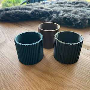 以下が含まれることがあります： リブ模様の円筒形の容器が3つあります。容器は茶色、濃い緑色、黒色です。