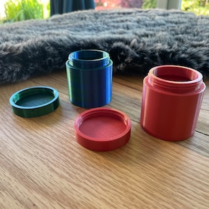 Op de afbeelding: Drie kleine containers met deksels. Eén container is blauw met een groen deksel, één is rood met een rood deksel en één is groen met een groen deksel.