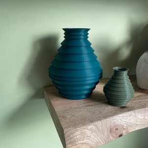 May include: Two teal and green ceramic vases with a ribbed design. The vases are sitting on a wooden shelf.
