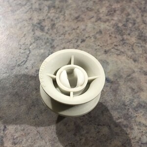 May include: A white plastic pulley with four spokes and a central hole. The pulley has a small white plastic ring inside the hole.
