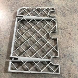 May include: A gray plastic shelf organizer with a diamond-shaped grid pattern. The shelf has three rows of slots for holding items.