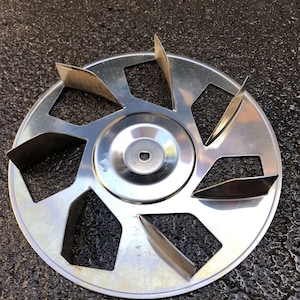 May include: A silver metal fan blade with seven blades. The fan blade is circular and has a centre hub.