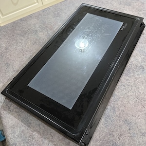 May include: Black microwave oven door with a clear glass panel and a white "remarkable" logo in the top right corner.