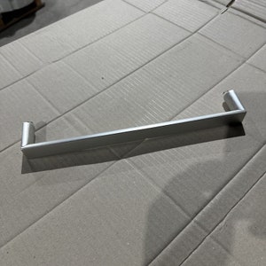 May include: A silver metal cabinet handle with a rectangular shape and rounded edges.