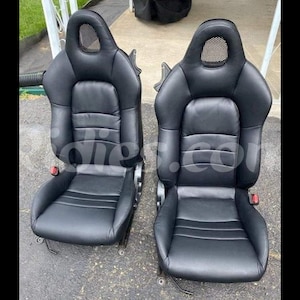 以下が含まれることがあります： メッシュヘッドレスト付きの黒い革の車のシート2つ。シートは、輪郭のある背もたれとパッド入りの底面を持つスポーティなデザインです。