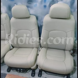 May include: Two beige leather car seats with headrests. The seats are in a car interior.