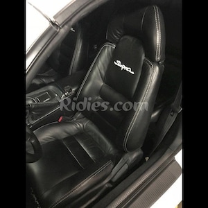 May include: Black leather car seats with white stitching and the word "Supra" embroidered on the driver's seat.