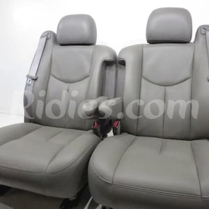 Puede incluir: Dos asientos de coche de cuero gris con reposacabezas y cinturones de seguridad. Los asientos tienen un reposabrazos de consola central.