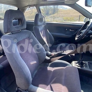 Könnte beinhalten: Das Innere eines Autos mit zwei grauen Stoffsitzen und einem braunen Lederlenkrad. Das Auto hat ein Schiebedach und ein graues Armaturenbrett.