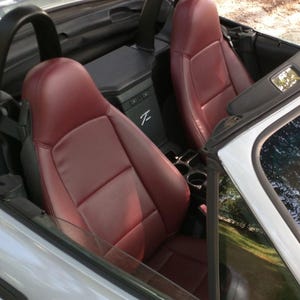 May include: A silver convertible car with two burgundy leather seats. The car has a black interior and a black roof.