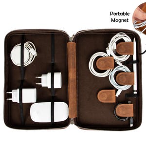 May include: A brown leather tech organizer with a zipper closure, holding various white tech accessories. Includes a wireless charger, power adapters, and cables secured with leather straps and magnetic cable organizers. The text "Portable Magnet" is visible.