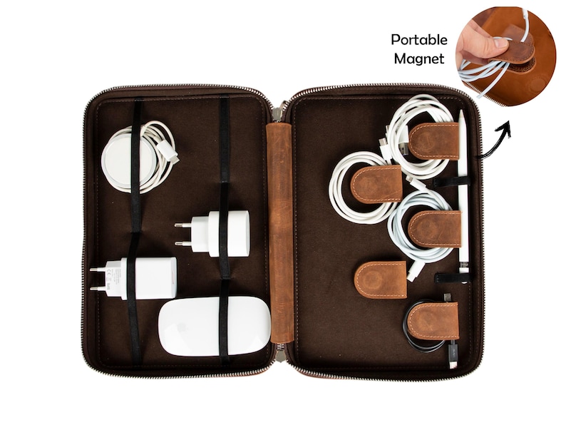 May include: A brown leather tech organizer with a zipper closure, holding various white tech accessories. Includes a wireless charger, power adapters, and cables secured with leather straps and magnetic cable organizers. The text "Portable Magnet" is visible.