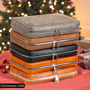 May include: A stack of zippered cases in various colors: grey, brown, black, shiny brown, and tan. Each case has a silver zipper. The cases are stacked on a red surface, with a Christmas tree in the background. The text "Perfect Christmas Gift" is at the bottom.