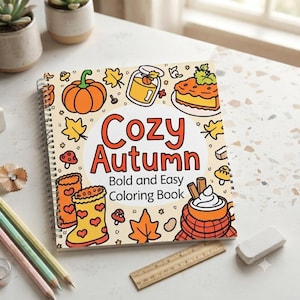 May include: A spiral-bound coloring book titled Cozy Autumn Bold and Easy Coloring Book, featuring a cream-colored cover with orange and yellow illustrations of pumpkins, autumn leaves, rain boots, a pie, and a mug of hot cocoa with whipped cream.