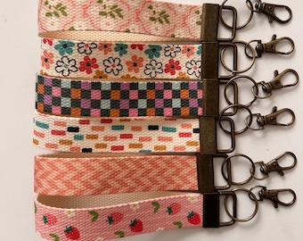 May include: Set of six colorful keychains with different patterns, including floral, checkered, and geometric designs. Each keychain features a metal ring and a lobster clasp.