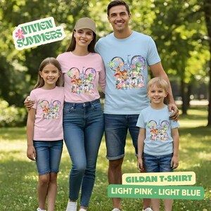 Puede incluir: Una familia de cuatro personas con camisetas Gildan rosa claro y azul claro a juego. Las camisetas presentan un dise&ntilde;o gr&aacute;fico colorido con personajes de dibujos animados. El texto "Vivien Summers" est&aacute; en un dise&ntilde;o verde y blanco.