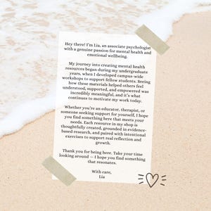 May include: A white rectangular card with text about mental health resources, held in place with tan tape on a sandy background. The text is in black and includes a heart symbol. The card is from Lia, an associate psychologist.