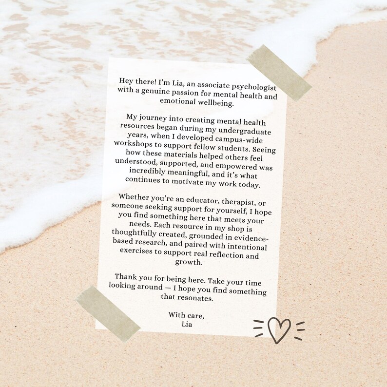 May include: A white rectangular card with text about mental health resources, held in place with tan tape on a sandy background. The text is in black and includes a heart symbol. The card is from Lia, an associate psychologist.