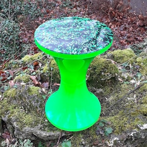 Op de afbeelding: Een groene en zwarte hars kruk met een uniek swirl-patroon op de bovenkant. De kruk heeft een brede basis en een smalle bovenkant.