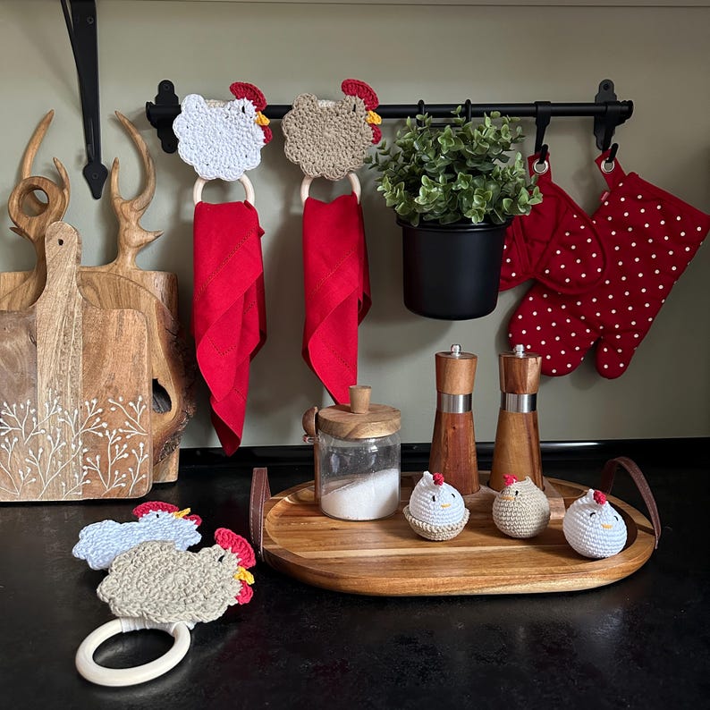 May include: A kitchen scene featuring a wooden tray with decorative crochet chickens, salt and pepper grinders, and a wooden-handled tray. Red napkins hang from a black rod with crochet chicken accents. Red oven mitts with white polka dots are also visible.