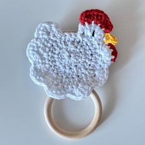 May include: A handmade crochet chicken-shaped baby teether. The chicken is white with a red comb and yellow beak. It has a wooden ring for easy gripping. A charming and safe toy for infants.
