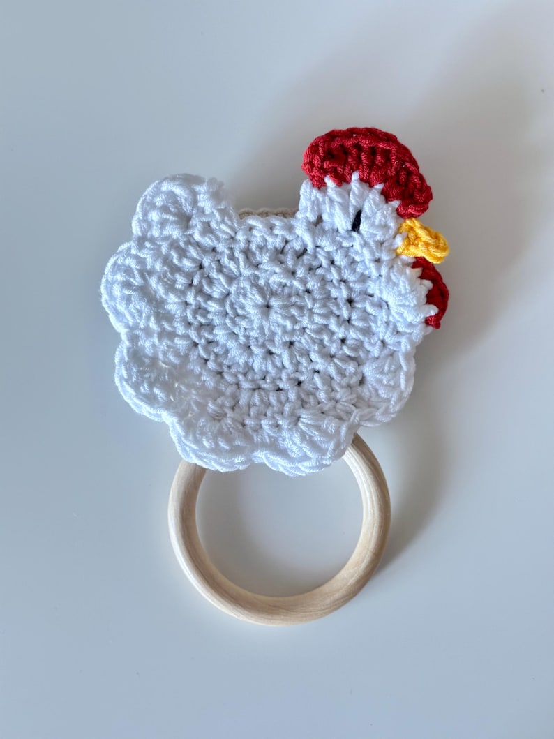 May include: A handmade crochet chicken-shaped baby teether. The chicken is white with a red comb and yellow beak. It has a wooden ring for easy gripping. A charming and safe toy for infants.