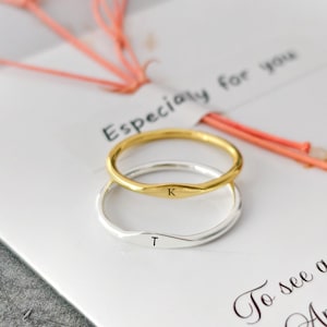May include: Two delicate rings, one gold and one silver, are stacked on a white card. The gold ring has the letter "K" engraved, while the silver ring has a "T". The card has the text "Especially for you" and a quote.