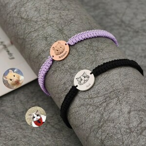 May include: Two personalized pet bracelets. One features a lavender braided band with a rose gold charm engraved with a hamster and the name "Nibbles." The other has a black band with a silver charm engraved with a cat and the name "Milo."