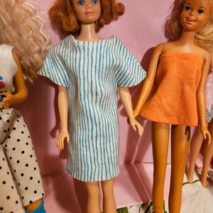 May include: Three vintage Barbie dolls with different hairstyles and outfits. The doll on the left is wearing a white shirt with black polka dots and blue pants. The doll in the center is wearing a blue and white striped dress. The doll on the right is wearing a peach-colored top and a white skirt.