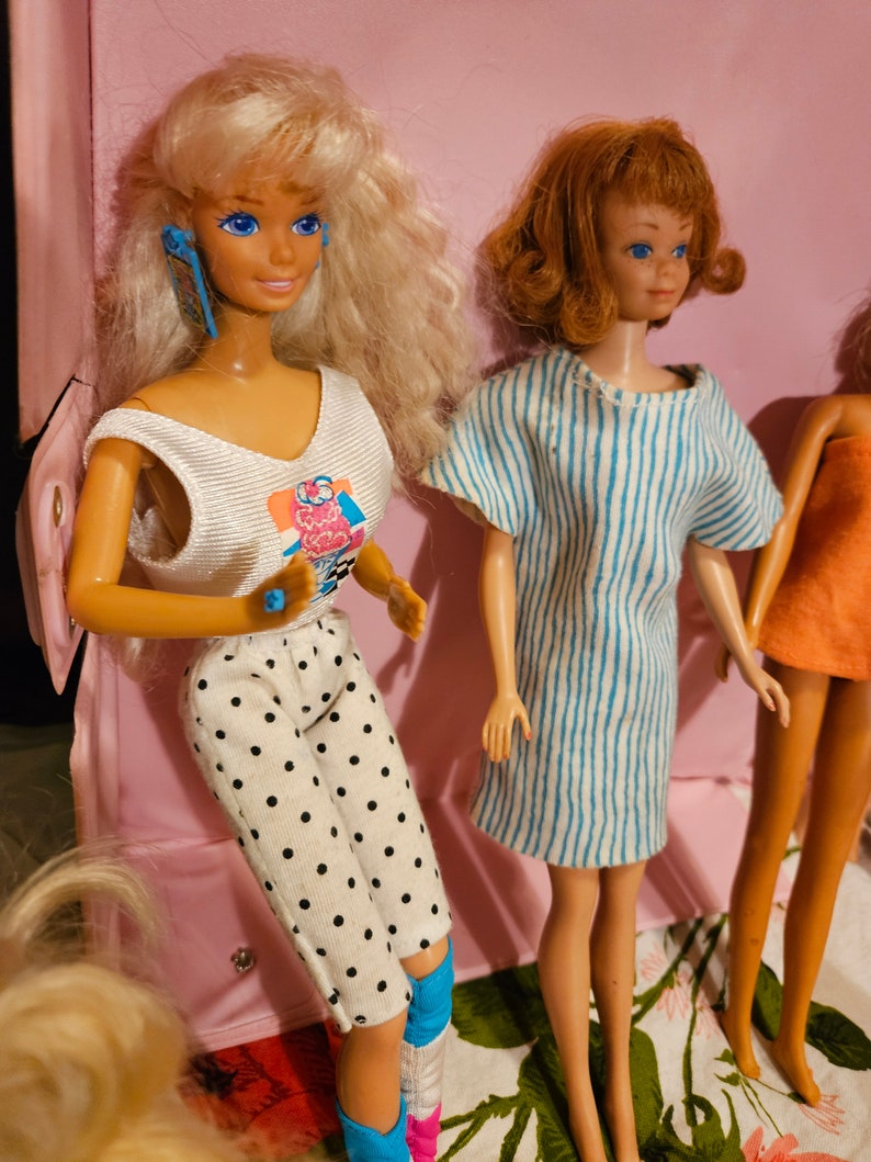 May include: Three vintage Barbie dolls with different hairstyles and outfits. The doll on the left has blonde hair, a white tank top with a colorful graphic, and black and white polka dot pants. The doll in the center has brown hair, a blue and white striped dress, and blue eyes. The doll on the right has blonde hair, a pink dress, and blue eyes.