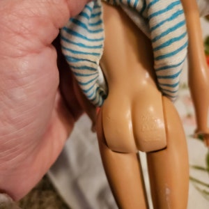 May include: A vintage Barbie doll with a blue and white striped shirt. The doll is missing her hair and has a visible seam on her leg.