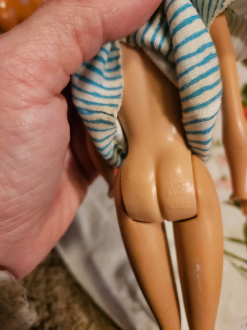 May include: A vintage Barbie doll with a blue and white striped shirt. The doll is missing her hair and has a visible seam on her leg.