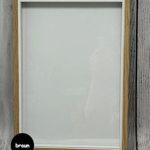 May include: A light brown wood picture frame with a white mat and a clear glass front. The frame is sitting on a white wood surface.