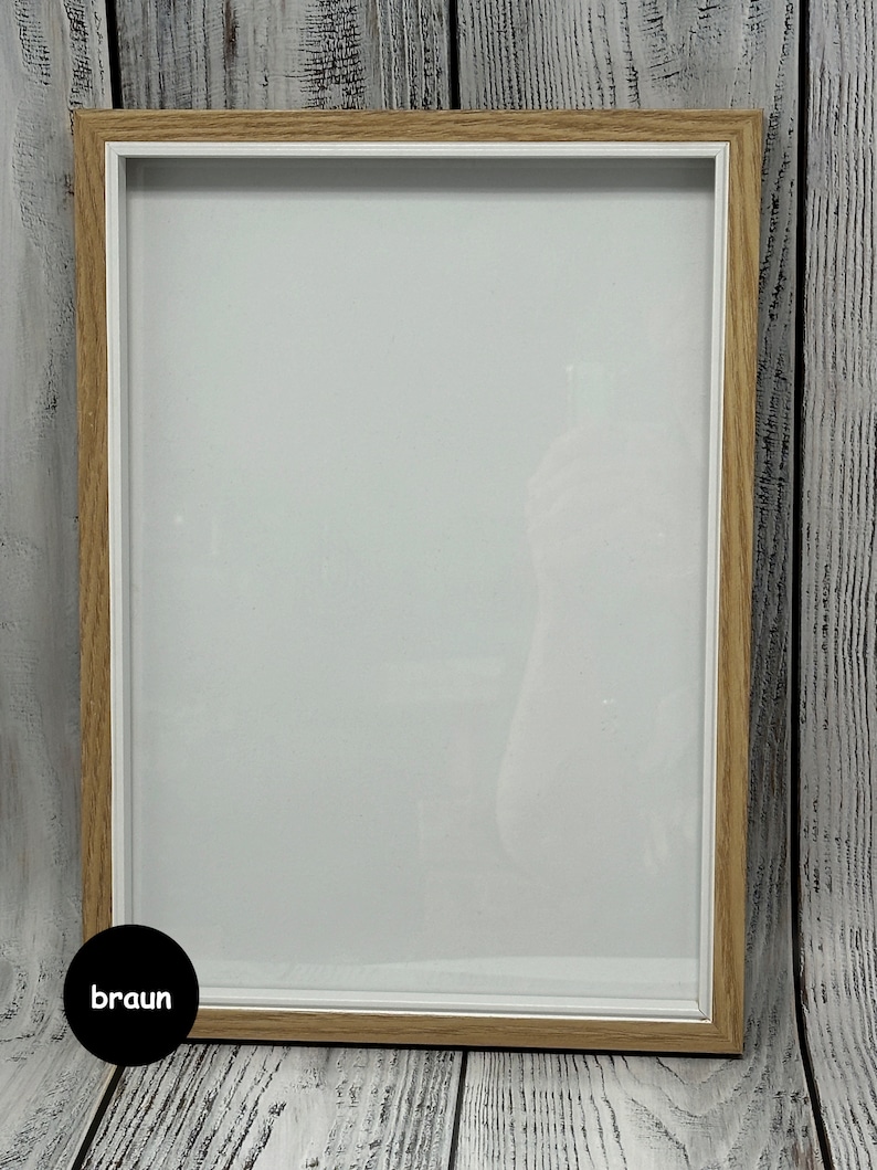 May include: A light brown wood picture frame with a white mat and a clear glass front. The frame is sitting on a white wood surface.