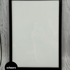 May include: A black picture frame with a white mat. The frame is on a whitewashed wood background. The word "schwarz" is written in black on a white circle in the lower left corner of the image.