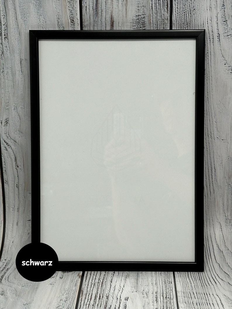 May include: A black picture frame with a white mat. The frame is on a whitewashed wood background. The word "schwarz" is written in black on a white circle in the lower left corner of the image.