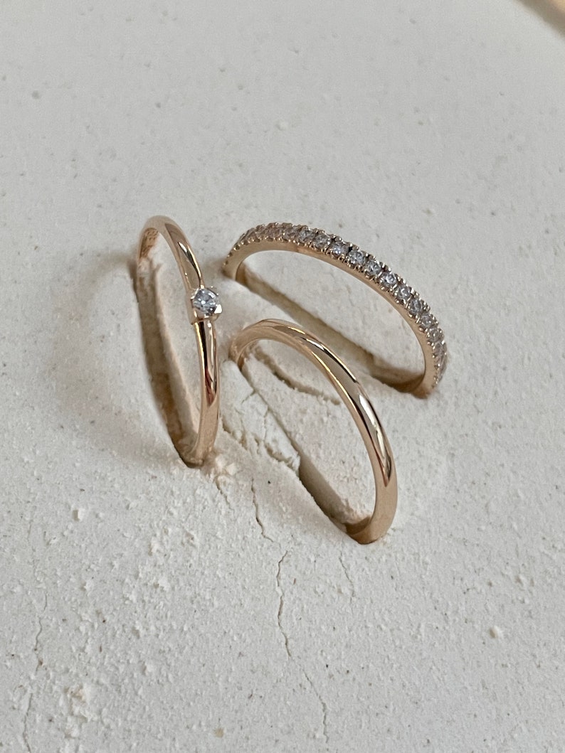 Pu&ograve; includere: Tre anelli d'oro con piccoli diamanti. L'anello superiore ha un solo diamante al centro. L'anello intermedio ha una fila di piccoli diamanti. L'anello inferiore &egrave; liscio.