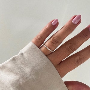 Pu&ograve; includere: Un delicato anello a fascia d'oro con una fila di piccole pietre preziose trasparenti.