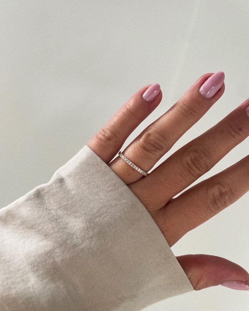 Pu&ograve; includere: Un delicato anello a fascia d'oro con una fila di piccole pietre preziose trasparenti.