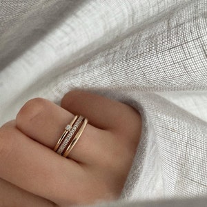 Pu&ograve; includere: Tre anelli d'oro impilati su un dito. L'anello superiore ha un piccolo diamante.