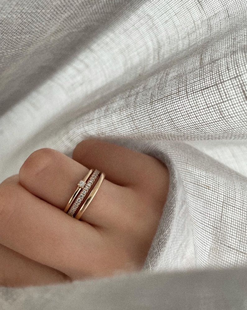 Pu&ograve; includere: Tre anelli d'oro impilati su un dito. L'anello superiore ha un piccolo diamante.