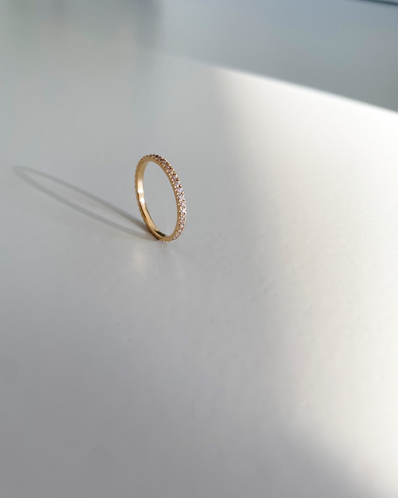 Pu&ograve; includere: Un sottile anello a fascia d'oro con piccole pietre trasparenti incastonate su tutta la fascia.