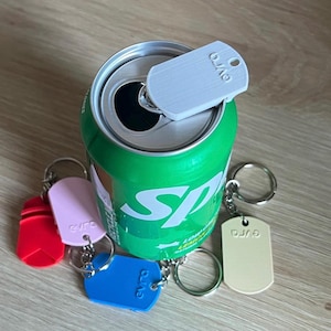 Puede incluir: Una lata verde de Sprite con una lengüeta blanca y varios llaveros de colores. Los llaveros son rojos, rosas, azules y beige, cada uno con un llavero plateado y el texto "gvro".