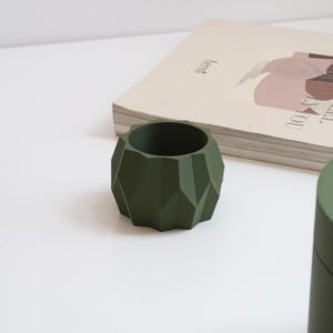 Pode incluir: Um vaso geométrico verde com um design facetado. O vaso é feito de um material liso e fosco.